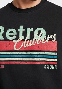 Schwarzer Sweatshirt mit strukturierter "Retro Clubbers" Grafik in Blau und Rot mit Risseffekt und horizontalen Streifen über "& SONS."