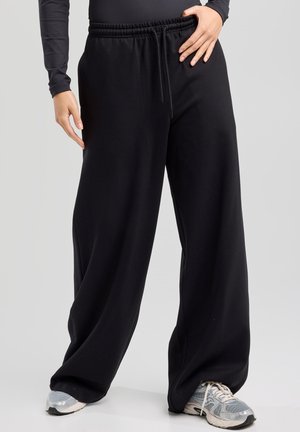 Black athletic pants with a wide leg design, elastic waistband, and drawstring. Made of soft fabric, featuring a smooth texture.
