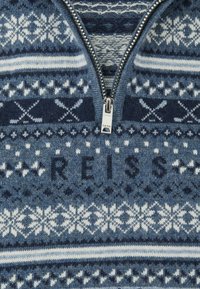 Sivi i plavi džemper od pletene tkanine s ovratnikom na patentni zatvarač. Ima geometrijske i pahuljaste uzorke, s "REISS" u tamnije plavoj boji.