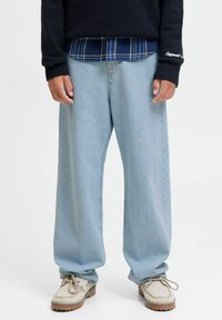 Lichtblauwe wijde spijkerbroek van denim, gecombineerd met een donkere gebreide trui en een geruit overhemd eronder. Geverfde crèmekleurige schoenen.