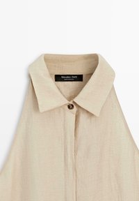 Beiges ärmelloses Leinenhemd mit spitzem Kragen und einer einzelnen braunen Knopfleiste am Ausschnitt, mit dem Etikett Massimo Dutti, hergestellt in Portugal.
