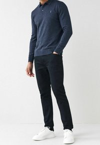 Marineblaue Langarm-Polohemd aus strukturiertem Stoff mit dezentem Logo, kombiniert mit schwarzen Slim-Fit-Hosen und weißen Sneakers.