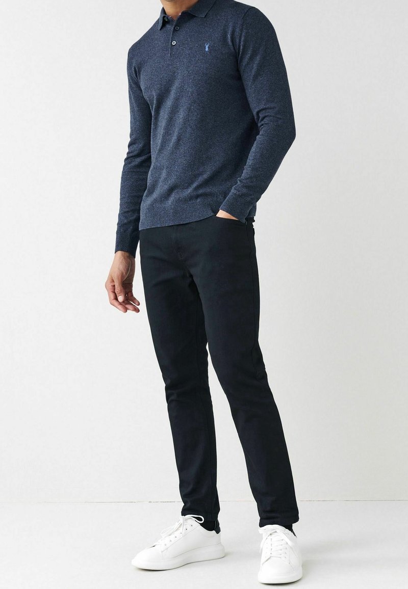 Marineblaue Langarm-Polohemd aus strukturiertem Stoff mit dezentem Logo, kombiniert mit schwarzen Slim-Fit-Hosen und weißen Sneakers.