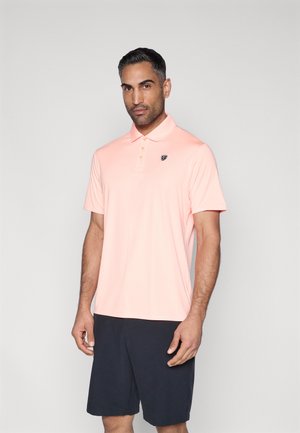 Polo rosa chiaro con collo e maniche corte, caratterizzata da tre bottoni e un piccolo logo sul lato sinistro del petto. Indossata con pantaloncini scuri.