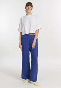 Witte crop t-shirt met opgerolde mouwen, gecombineerd met losse blauwe broeken en witte sneakers. Soepele stof en een relaxte pasvorm.