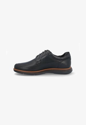 Zapato de cuero negro con puntera redondeada, seis ojales, detalles de costura y una suela de goma marrón en contraste.