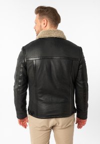 Zwarte leren jas met een gestructureerde afwerking, voorzien van een beige schapenvachtkraag en slanke zijnaad, vastgemaakt in de taille met verstelbare riemen.