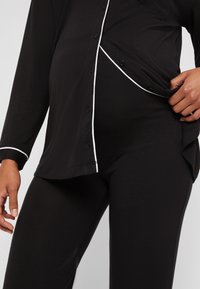 Svart lounge-set bestående av en långärmad skjorta med knappar och vit kantning samt matchande leggings, tillverkad av mjukt, elastiskt tyg.