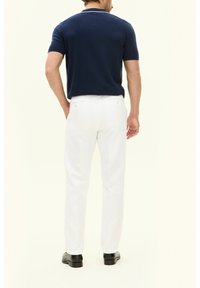 Marineblauw overhemd met korte mouwen, gecombineerd met een witte broek met een rechte snit. Het geheel wordt afgemaakt met zwarte nette schoenen.