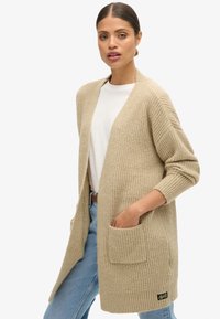 Beige strikket cardigan med lange ærmer, åbent front og to forreste lommer. Har ribbet tekstur og et mærketags ved den nedre kant.