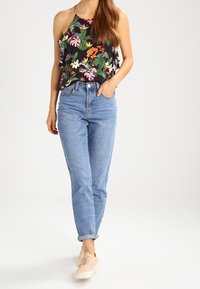 Top a fascia floreale con bordi arricciati, base nera e colori vivaci; abbinato a jeans dritti blu chiaro e sneakers rosa chiaro.
