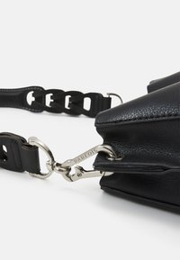 Svart läderhandväska med texturerad yta, avtagbart kedjestraps och silverfärgad metall. Har blixtlåsstängning och logotypdetalj.