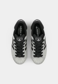 Black and gray Adidas sneakers with a textured rubber toe cap, flat laces, and three black stripes on each side. Detailing includes a logo on the tongue.