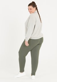 Lys grå oversized sweatshirt med ribbet kant kombineret med olivengrønne tapered joggers, begge i blødt stof, suppleret med hvide sneakers.