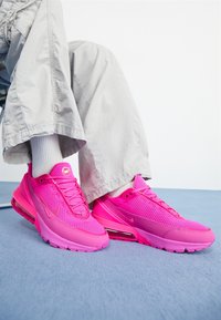 Klart rosa träningssneakers med ovandel i mesh, släta detaljer och synlig dämpningsenhet. I kombination med ljusgrå byxor och vita strumpor.