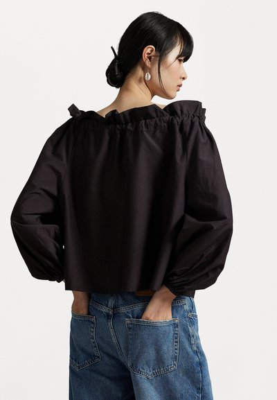 Black cropped blouse with ruffled neckline and voluminous sleeves, paired with blue denim jeans featuring large back pockets.