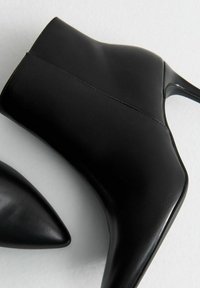 Botas de cuero negro hasta el tobillo con punta afilada y un elegante tacón de aguja, acentuadas por costuras sutiles y una textura suave.