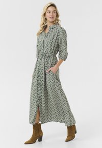 Maxiklänning i ett grönt blommönster; knäppt design, åtsittande midja, två sidofickor och sidoklyfta; matchad med bruna mocka ankelstövlar.