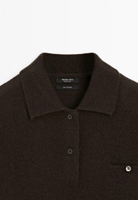 Polo shirt in cashmere marrone scuro caratterizzato da un colletto, tre bottoni e una tasca sul petto con dettaglio a bottone arrotondato. Texture morbida e scollatura a coste.
