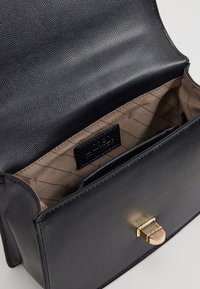 Černá kožená kabelka s texturovaným povrchem, zlatým kováním a béžovou vzorovanou podšívkou. Obsahuje jeden oddíl.