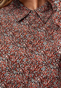 Chemise à boutons avec un motif abstrait coloré en rouge, noir et blanc. Design avec col, texture lisse et léger éclat.