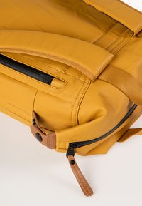 Zaino giallo con una finitura liscia e opaca, dotato di cerniere nere, dettagli beige e spallacci imbottiti per il massimo comfort.