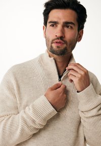 Stickad tröja i ljusbeige med halvdragkedja, ribbat mönster och långa ärmar, som visar en avslappnad design.