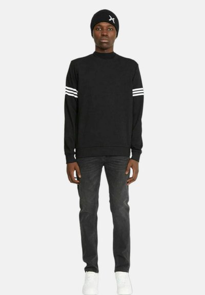 Felpa nera con strisce bianche sulle maniche, abbinata a jeans scuri e sneakers bianche. Chi la indossa ha anche un berretto nero.