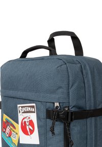 Dark blue fabric backpack with black straps, featuring Superman patches and a side buckle. Smooth texture and rectangular shape.