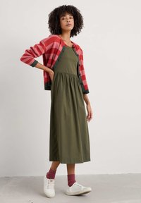 Röd- och rosa randig cardigan över en olivgrön klänning med midjesöm och en flödande design. Vita sneakers med vinröda strumpor.