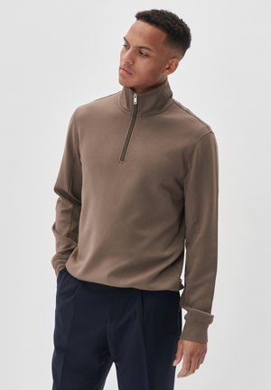 Suéter marrón con media cremallera y mangas largas, de textura suave y con detalles mínimos de costura, combinado con pantalones azul marino.