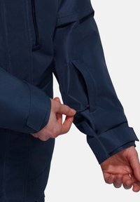 Marineblauer wasserdichter Jacke mit einer Reißverschlusstasche am Arm und verstellbaren Ärmelbündchen. Hoher Komfort und durchdachtes Design für Funktionalität.
