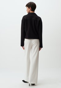 Zwarte cropped sweatshirt met een kraag, voorzien van lange mouwen en een gladde textuur, gecombineerd met witte wijdlopende broeken en zwarte hakken.