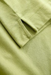 Groene katoenstof met een gevouwen rand en stikdetails. Glad van textuur, met een lichte glans, en een schoon, eenvoudig ontwerp.