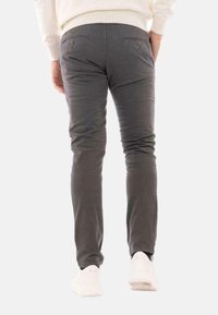 Pantaloni grigi slim-fit con una texture liscia, dotati di due tasche posteriori con chiusura a bottone. Abbinati a sneakers bianche.