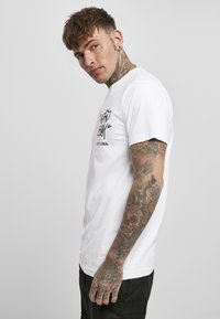 White cotton t-shirt with black graphic text and logo, short sleeves, crew neck, and relaxed fit. Features detailed tattoos on the arm.