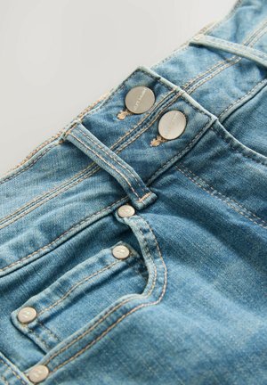 I jeans in denim blu chiaro hanno una vita alta, due bottoni argentati e una piccola tasca frontale. Le cuciture visibili aggiungono texture e dettaglio.