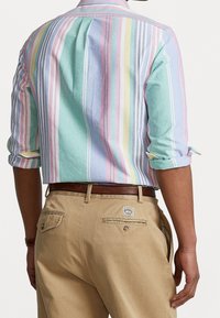 Camisa de manga corta a rayas multicolores en tonos pastel, con un ajuste relajado y mangas dobladas. Combinada con pantalones marrones claros que cuentan con bolsillos traseros.