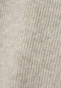 Tessuto lavorato a maglia beige con una superficie morbida e testurizzata. Presenta un motivo a coste con variazioni di tonalità chiare e scure.