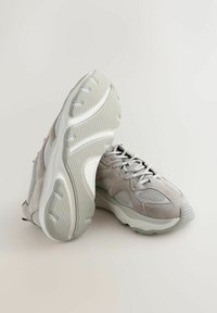 Hellgraue Sneakers aus einer Mischung von Wildleder und Netzmaterialien, mit strukturierten Gummisohlen und flachen Schnürsenkeln. Abgerundete Zehenform mit Polsterung.