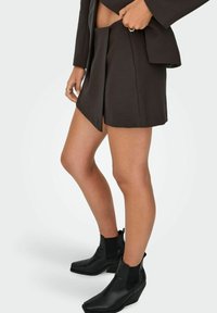 Juodas pritaikytas mini sijonas su plišais, derinamas su juodais auliniais batais su platforma ir elastingomis šoninėmis juostelėmis.