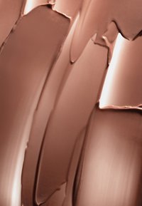 Tourbillons lisses de fond de teint liquide taupe crémeux avec des reflets brillants en gros plan.
