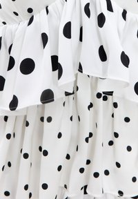 Tissu blanc à pois noirs avec volants superposés et détail élastique froncé, affichant un motif fluide et texturé.