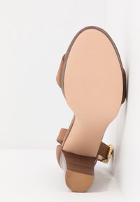 Sandale en cuir marron avec un talon bloc et une sangle à la cheville, vue de la semelle sur fond blanc.