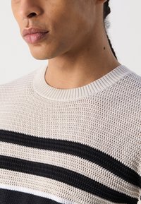 Strickpullover mit einer hellbeigen Textur, schwarzen und weißen horizontalen Streifen sowie einem gerippten Rundhalsausschnitt.