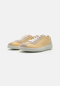 Sneakers gialle in pelle con dettagli in suede beige, lacci bianchi e suola in gomma con texture. Punta arrotondata e design casual a profilo basso.