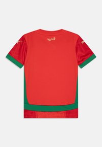 Červený športový dres s zelenými detailmi, ktorý má štruktúrovaný červený dizajn na rukávoch a nápis „المغرب“ v zlate na chrbte.