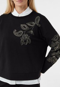 Czarna bluza z finezyjną srebrną aplikacją z koralików w kwiatowe wzory na rękawach, o luźnym kroju i miękkiej fakturze.