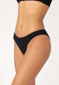 Czarny dół bikini o teksturowanym wzorze, w niskim kroju i minimalnym zakryciu. Tkanina wydaje się elastyczna i gładka.
