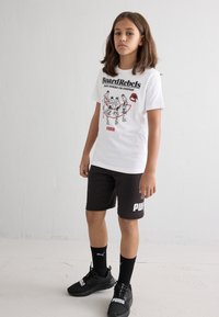 Hvit bomulls t-skjorte med svart grafisk trykk og røde detaljer, parret med svarte shorts med hvit logo, svarte joggesko og svarte sokker.